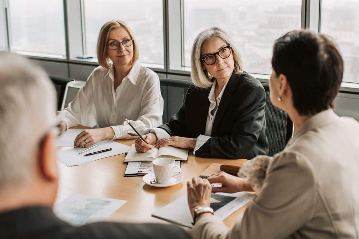 Four people are seated at a conference table during a meeting, discussing with documents.