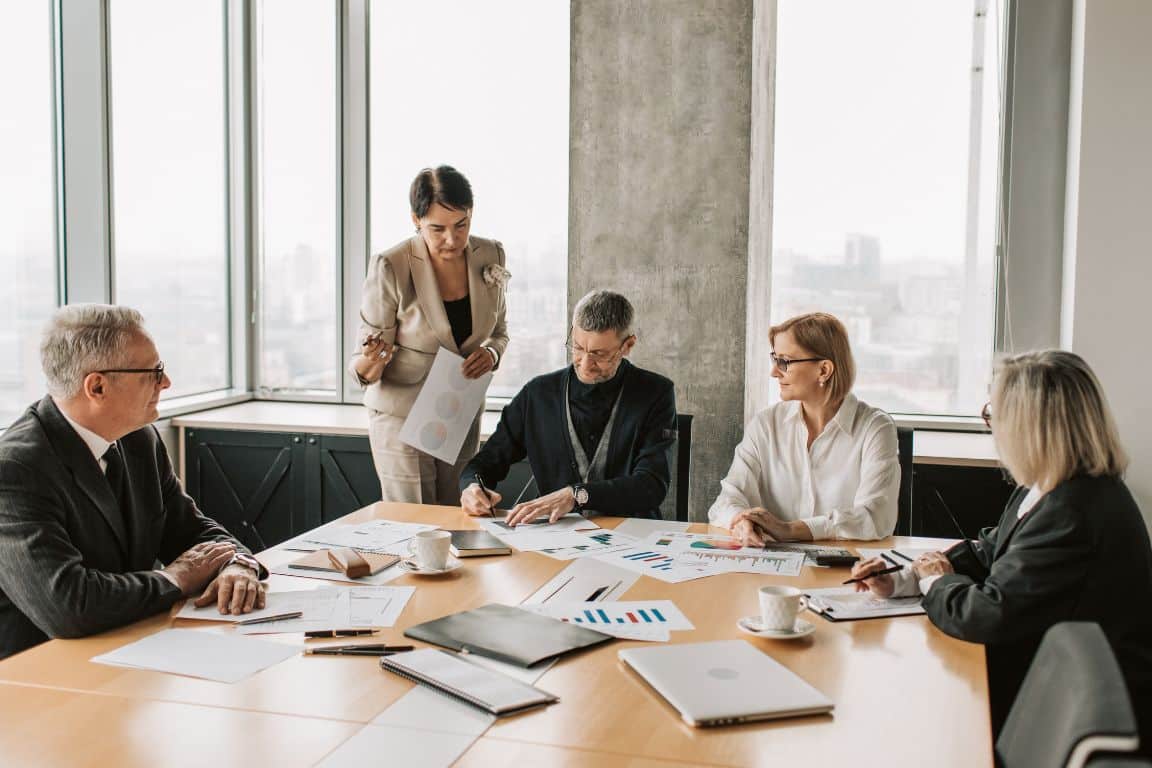 A group of business professionals engaged in a discussion around a conference table in a modern meeting room.