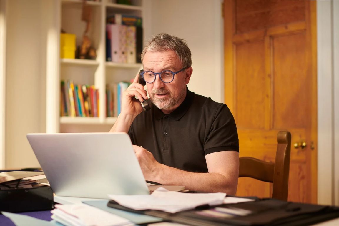 Man sitting at his laptop talking on the phone.